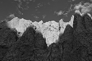 The first light of sunrise illuminates the erie rock formations deep in Badlands National Park as a waning moon gentle descends behind. - South Dakota Photograph