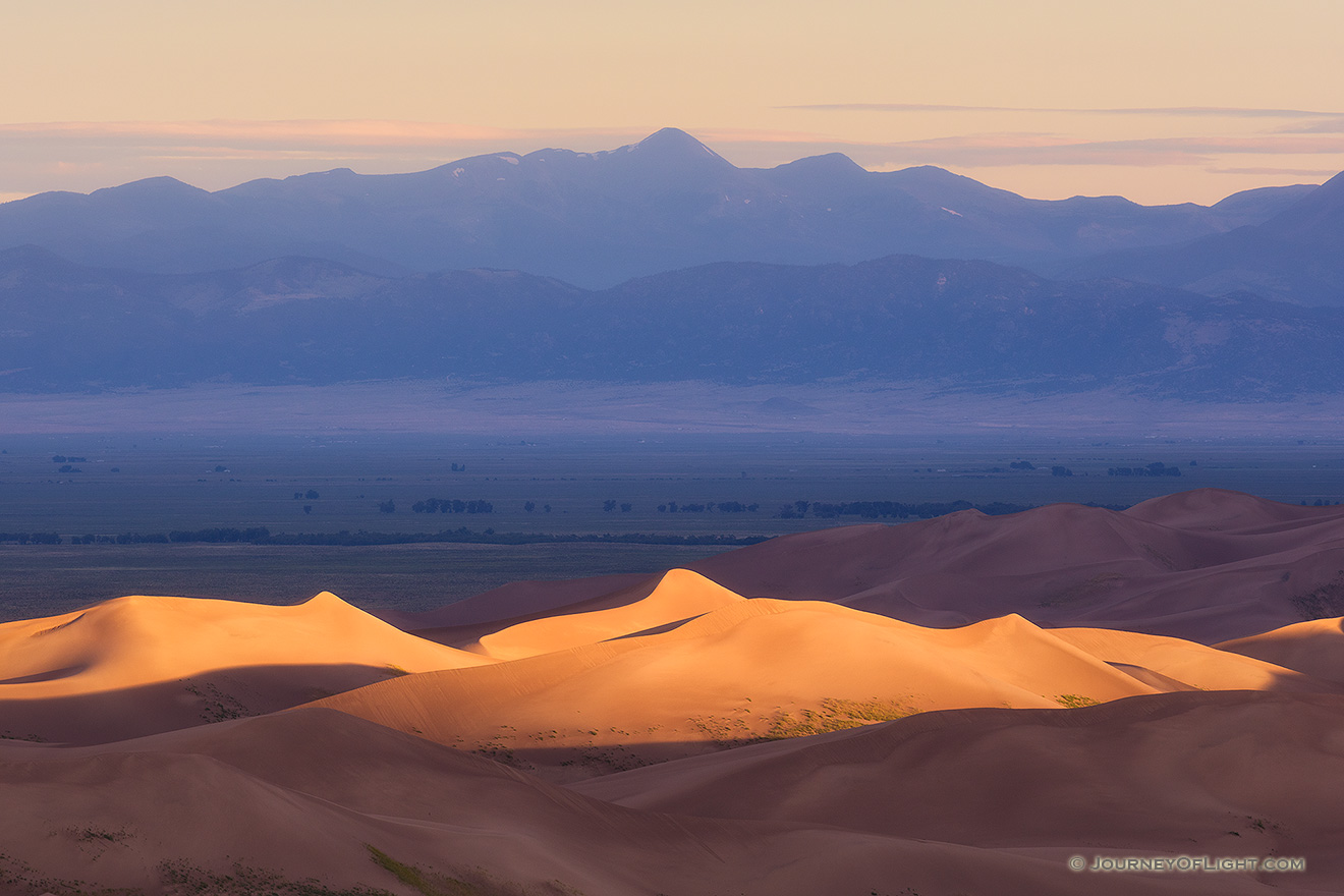 Light graces the tops of the Sand Dunes in the distance as the sun peaks over the Sangre De Cristo range.