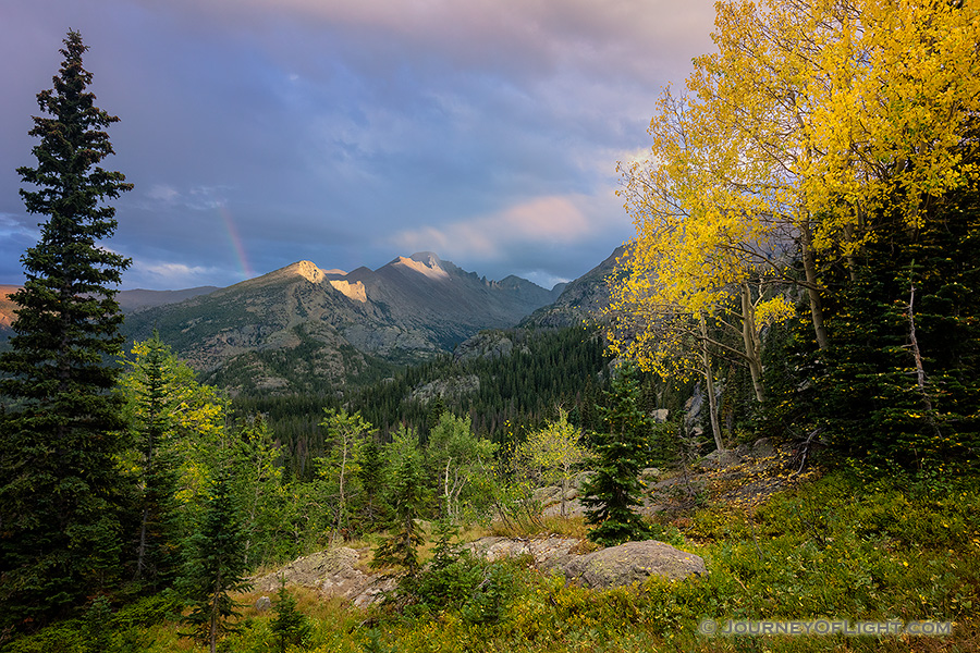 On a cool autumn evening sun strikes the peak of Long's Peak in Rocky Mountain National Park. A faint rainbow briefly appeared as the storm moved over the mountain. - Colorado Photography