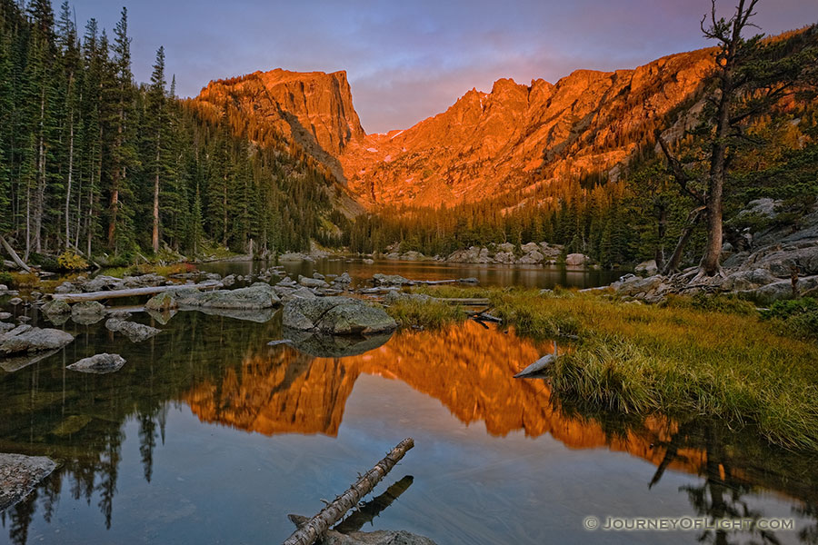 Still and peaceful, Dream Lake in Rocky Mountain National Park reflects an image of the majestic Hallett Peak while it glows red with the light of the rising sun. - Rocky Mountain NP Photography