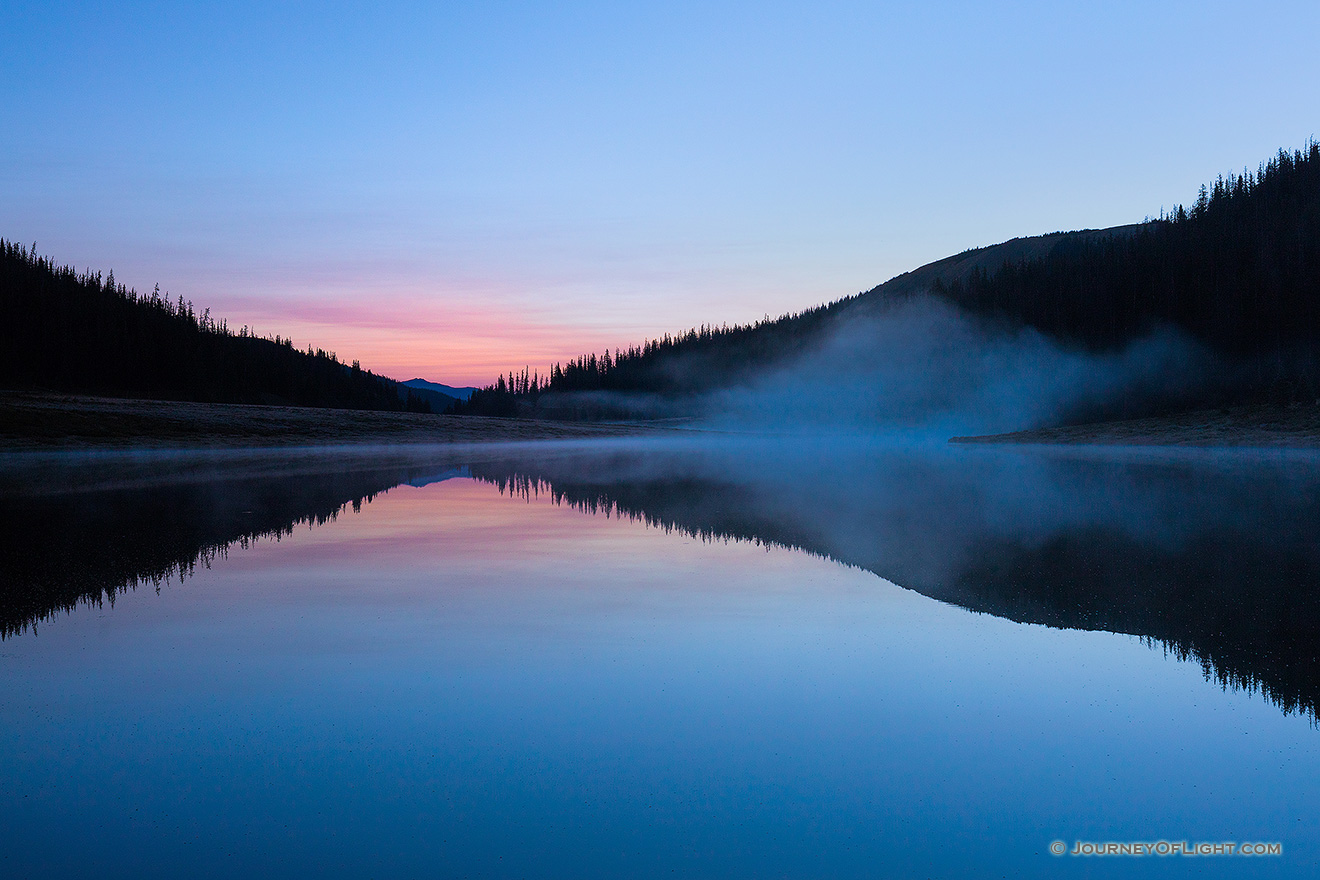 While a hint of red glows in the distance, cool blue hues dominate the sky just before sunrise over Poudre Lake in Rocky Mountain National Park. - Colorado Picture