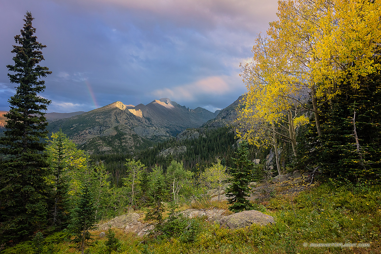 On a cool autumn evening sun strikes the peak of Long's Peak in Rocky Mountain National Park.  A faint rainbow briefly appeared as the storm moved over the mountain. - Colorado Picture