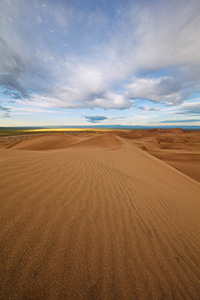 Dunes flow into the west at Great Sand Dunes National Park as white clouds lazily float above. - Colorado Landscape Photograph