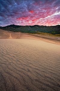 Early morning on the Great Sand Dunes after a stormy night brought clouds that reflected intense warm hues from the rising sun.  I had envisaged a photograph like this at the sand dunes for over a year, capturing the the texture of the dunes, the sweeping lines that lead to the Sangre de Cristo mountains, with a brillant sunrise. - Colorado Photograph