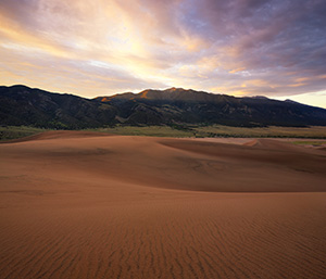 Sunlight streams through a pass in the Sangre de Cristo Mountains and illuminates the peak of Carbonate Mountain just southeast of the dunes at Great Sand Dune National Park. - Colorado Photograph