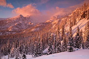 Sunlight illuminates the freshly fallen snow and the trees in the valley while Long's Peak is partially hidden by the blowing snow and clouds. - Colorado Landscape Photograph