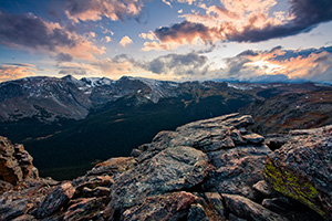 The setting sun streams through the clouds, illuminating the peaks of Rocky Mountain National Park and the valley below. - Colorado Photograph