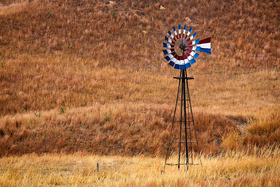 A scenic landscape photograph of a windmill painted red, white, and blue in the sandhills of Nebraska. - Nebraska Photography