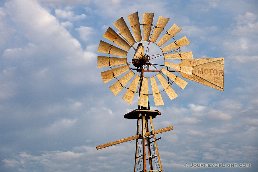 In rural Dixon County in Northeastern Nebraska a still windmill reflects the golden light of the rising sun against a cloudy sky. - Nebraska Photography