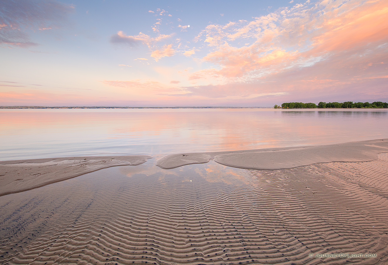 A beautiful dawn over Lake McConaughy in western Nebraska illuminates clouds with bright pink hues as they float lazily in front of the moon. - Sandhills Picture