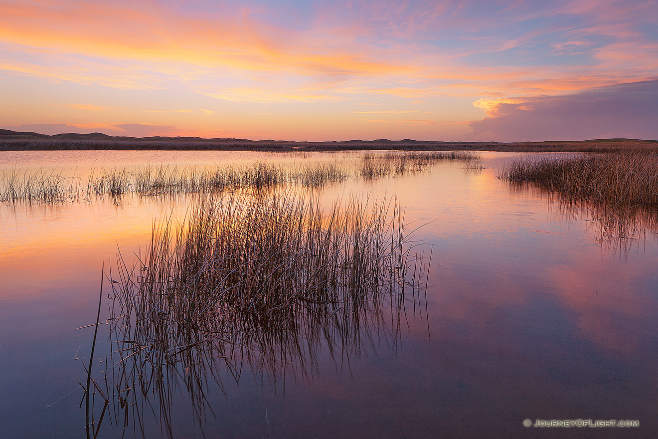 On a cool and quiet spring evening, the sun illuminates the clouds hanging over Perrin Lake at Crescent Lake National Wildlife Refuge in the Sandhills of Nebraska.  Pinks and Oranges reflected in the lake as ducks quacked in the distance. - Nebraska Picture