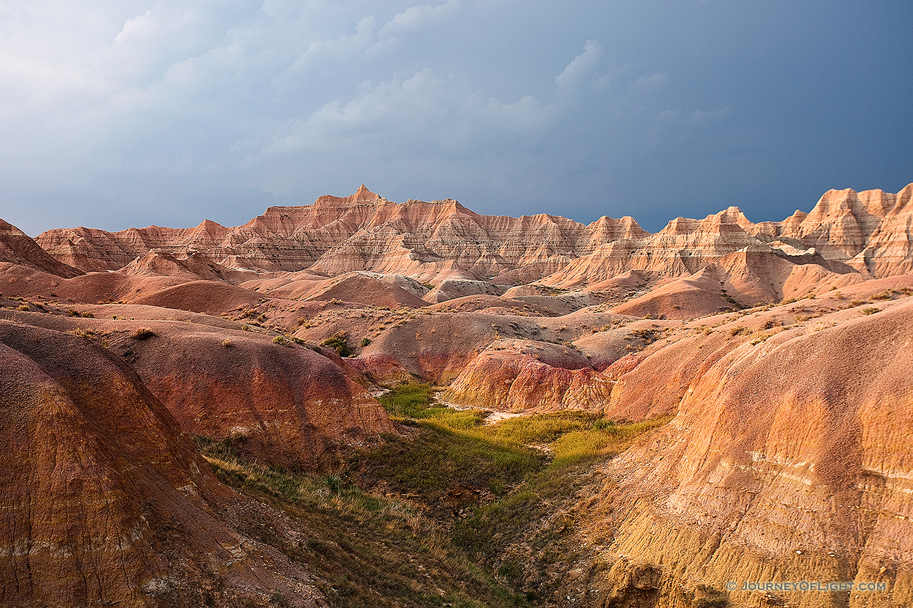One of the things that I can say about visiting <a href='http://www.journeyoflight.com/journey12/photo-keyword-sort.asp?keywordselected=Badlands National Park'>Badlands National Park</a> in <a href='http://www.journeyoflight.com/journey12/photo-keyword-sort.asp?keywordselected=South Dakota'>South Dakota</a> is that the weather is almost always very dynamic when I am there.  I rarely have times when it is all sunny or all cloudy.  Usually, when the sun bursts forth there is some great color in the sky.  During the day clouds lazily float by and then in the afternoon I am often treated to a spectacular storm.  This image is from one such evening, a summer storm was rolling through and the sunlight was streaming through the clouds illuminating the badlands landscape. - South Dakota Picture