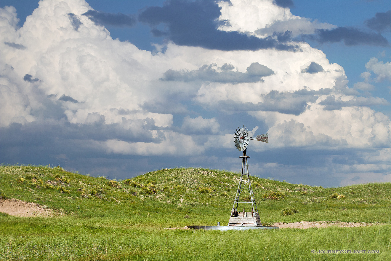 The sun shines on a windmill deep within the Sandhills of Nebraska as storm clouds roll in the distance. - Nebraska Picture