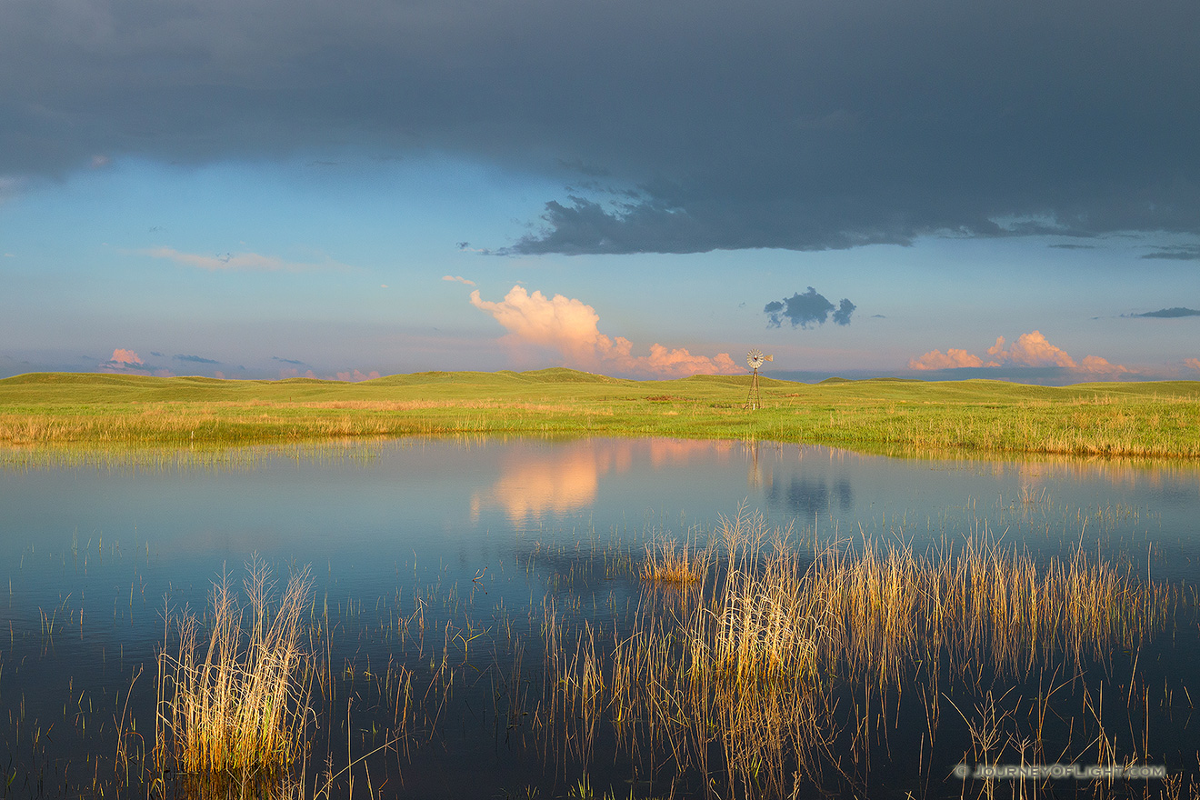 A windmill and storm clouds are reflected in a small lake in the Sandhills of Nebraska. - Nebraska Picture