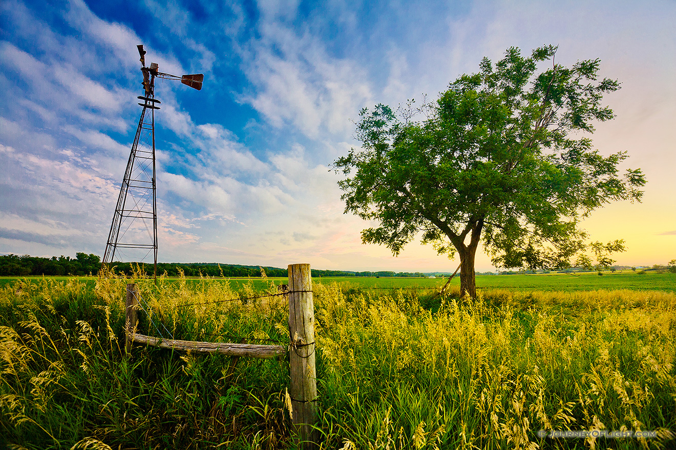 An old windmill and fence are the only company to a single tree on the eastern Nebraska plains. - Nebraska Picture