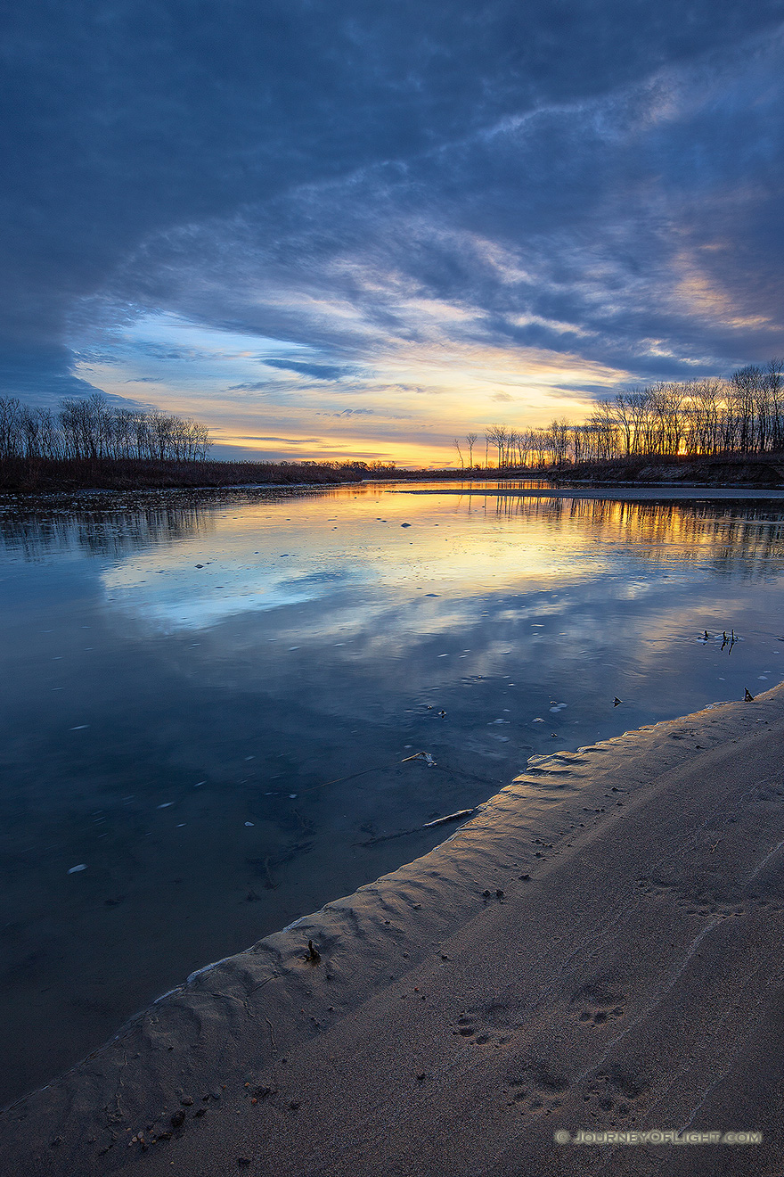 Paw prints from a raccoon are illuminated on the shore as the sun rises over the Missouri River at Ponca State Park in northeastern Nebraska. - Ponca SP Picture