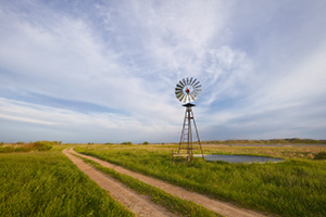 In an area of the Sandhills of Nebraska, far from civilization a two-track road meanders by a windmill and a lake nestled in the hills. - Nebraska Sandhills Photograph