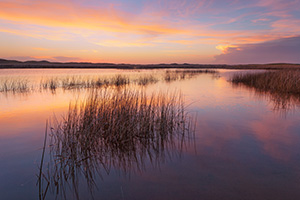 On a cool and quiet spring evening, the sun illuminates the clouds hanging over Perrin Lake at Crescent Lake National Wildlife Refuge in the Sandhills of Nebraska.  Pinks and Oranges reflected in the lake as ducks quacked in the distance. - Nebraska Nature Photograph