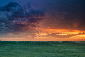 The verdant prairie grass appears as a green carpet in the valleys of Agate Fossil Beds National Monument in western Nebraska as the last bit of sunlight radiates from beneath the dark storm clouds.  From a high perch, I watched this storm as it moved past, the clouds changing and morphing. - Nebraska Landscape Photograph