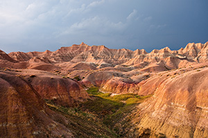 One of the things that I can say about visiting <a href='http://www.journeyoflight.com/journey12/photo-keyword-sort.asp?keywordselected=Badlands National Park'>Badlands National Park</a> in <a href='http://www.journeyoflight.com/journey12/photo-keyword-sort.asp?keywordselected=South Dakota'>South Dakota</a> is that the weather is almost always very dynamic when I am there.  I rarely have times when it is all sunny or all cloudy.  Usually, when the sun bursts forth there is some great color in the sky.  During the day clouds lazily float by and then in the afternoon I am often treated to a spectacular storm.  This image is from one such evening, a summer storm was rolling through and the sunlight was streaming through the clouds illuminating the badlands landscape. - South Dakota Photograph