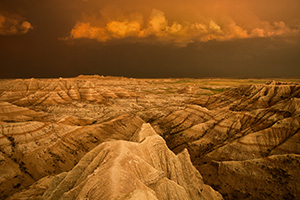 Facing east, the sky was nearly pitch black shrouded by the fierce storm that had just passed through.  As the sun dipped below the horizon the last rays hit the trailing storm clouds and the ambient warm light lit up the valley across the Badlands in South Dakota. - South Dakota Photograph
