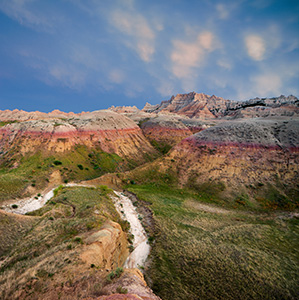 On a warm summer evening as I was photographing Badlands National Park in South Dakota, I could hear thunder in the distance.  As I continued to capture the landscape a patch of mammantus clouds began to creep closer.  Generally associated with severe thunderstorms, I began to get my gear ready in case things turned bad and I had to leave quickly.  Luckily, the wind shifted and the storm began to move away, just at the last light of day began to peak through the remaining clouds in the west illuminating the landscape. - South Dakota Landscape Photograph