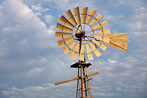 In rural Dixon County in Northeastern Nebraska a still windmill reflects the golden light of the rising sun against a cloudy sky. - Nebraska Photograph