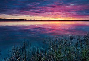 A small lake nestled in the Sandhills reflects the rising sun on a cool spring morning. - Nebraska Photograph