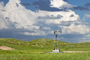 The sun shines on a windmill deep within the Sandhills of Nebraska as storm clouds roll in the distance. - Nebraska Photograph