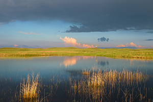 A windmill and storm clouds are reflected in a small lake in the Sandhills of Nebraska. - Nebraska Photograph