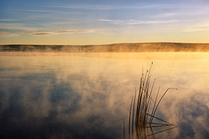 One of the most expansive and uninhabited areas of Nebraska also holds expansive beauty.  The Oglala National Grasslands in northwestern Nebraska represent some of the last native grasslands in the United States.  On a cool September morning a few years ago, I ventured out to the Meng Reservoir and captured the morning sun hitting the mist rising from the water.  The only sound was ducks quacking the distance welcoming the new day. - Nebraska Photograph