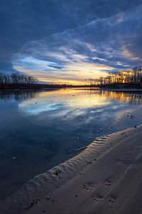 Paw prints from a raccoon are illuminated on the shore as the sun rises over the Missouri River at Ponca State Park in northeastern Nebraska. - Nebraska Landscape Photograph