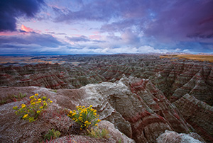 On a cool morning, the smell of a past rain fills the air.  The sunrise illuminates the passing storm clouds at Badlands National Park, South Dakota. - South Dakota Photograph