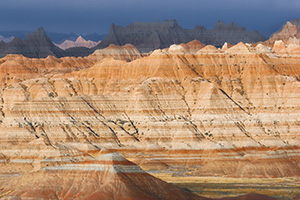 As a storm clears over the badlands light from the sun illuminates the rock formations while the dark clouds still dominate the sky in the distance. - South Dakota Photograph