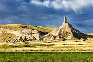 The spire known as Chimney Rock glows warm in the recent sunrise and the surrounding fields are a verdant green from a recent rain. - Nebraska Photograph