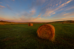 A scenic landscape photograph of hay bales and a beautiful glow in the sandhills of Nebraska. - Nebraska Photograph