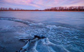In early winter, sunrise hits the landscape illuminating the forming ice on the lake at DeSoto National Wildlife Refuge.