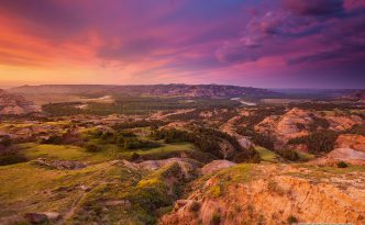 Above a bend in the Little Missouri River in the North Unit of Theodore Roosevelt National Park, clouds glow purple and orange as the sun just begins to rise above the horizon.