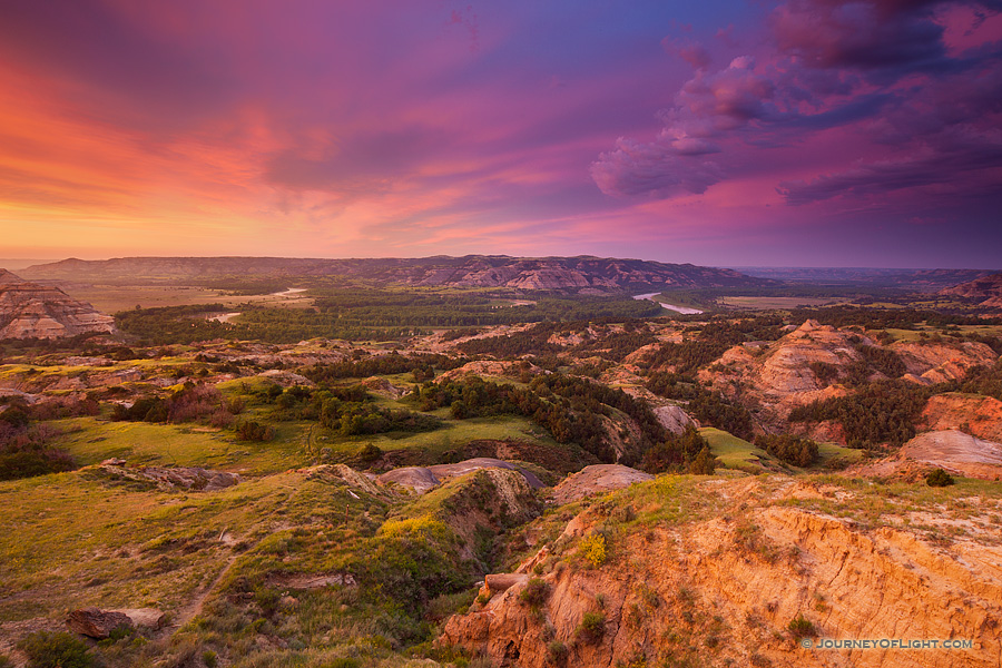 Above a bend in the Little Missouri River in the North Unit of Theodore Roosevelt National Park, clouds glow purple and orange as the sun just begins to rise above the horizon.