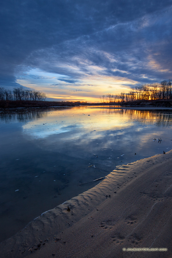 Pawprints from a racoon are illuminated on the shore as the sun rises over the Missouri River at Ponca State Park in northeastern Nebraska.