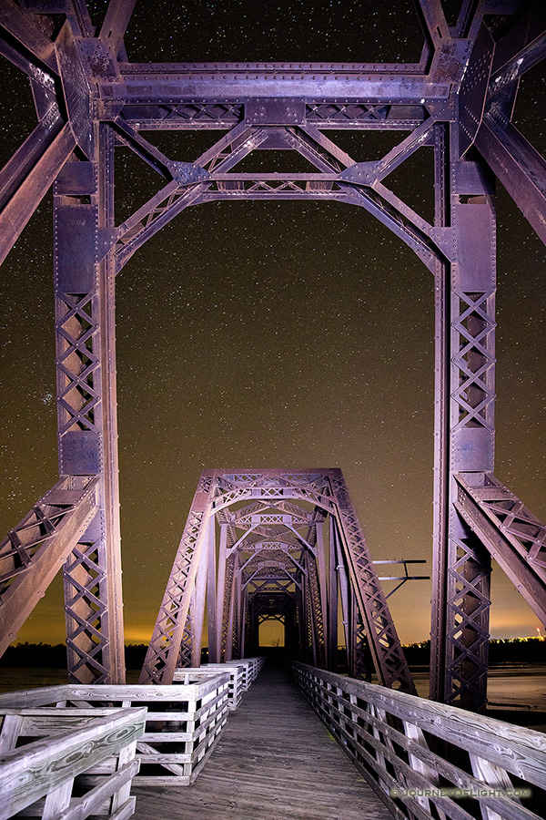 On a clear night at Niobrara State Park, I setup on the railroad trussle converted to a footbridge near the confluence of the Niobrara and Missouri Rivers. Using a flashlight I lightpainted the bridge while exposing for the stars. In the distance the lights of Niobrara can be seen glowing on the horizon.