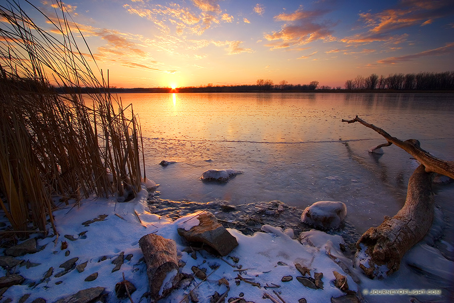 The warm setting sun shines brightly across the frozen lake before dipping below the horizon. On a cold February evening in 2006 I ventured to DeSoto Wildlife Refuge looking to photograph the Bald Eagles that nest here in the winter. What I found was a gorgeous sunset.