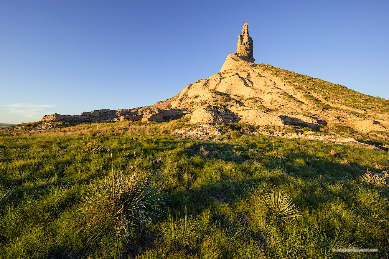 To the west of Chimney Rock the sky glows warm with the light of the setting sun.