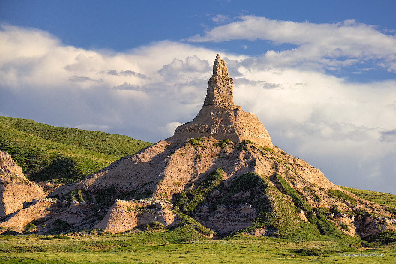 Clouds gather behind Chimney Rock as the glow of the late afternoon sun illuminates its western side.