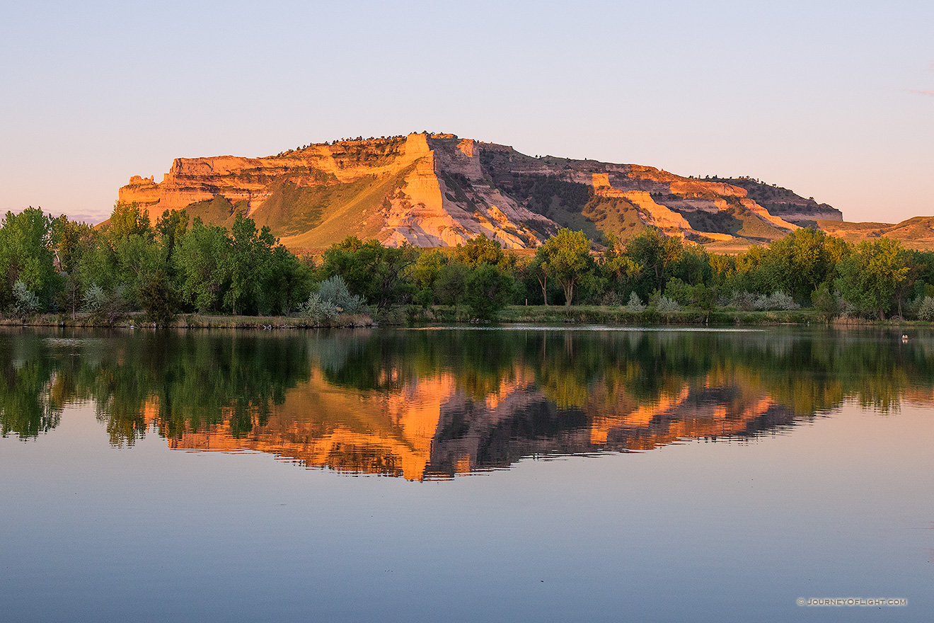 Glowing in the light of the recently risen sun, Scotts Bluff National Monument in western Nebraska is reflected in a small nearby lake.