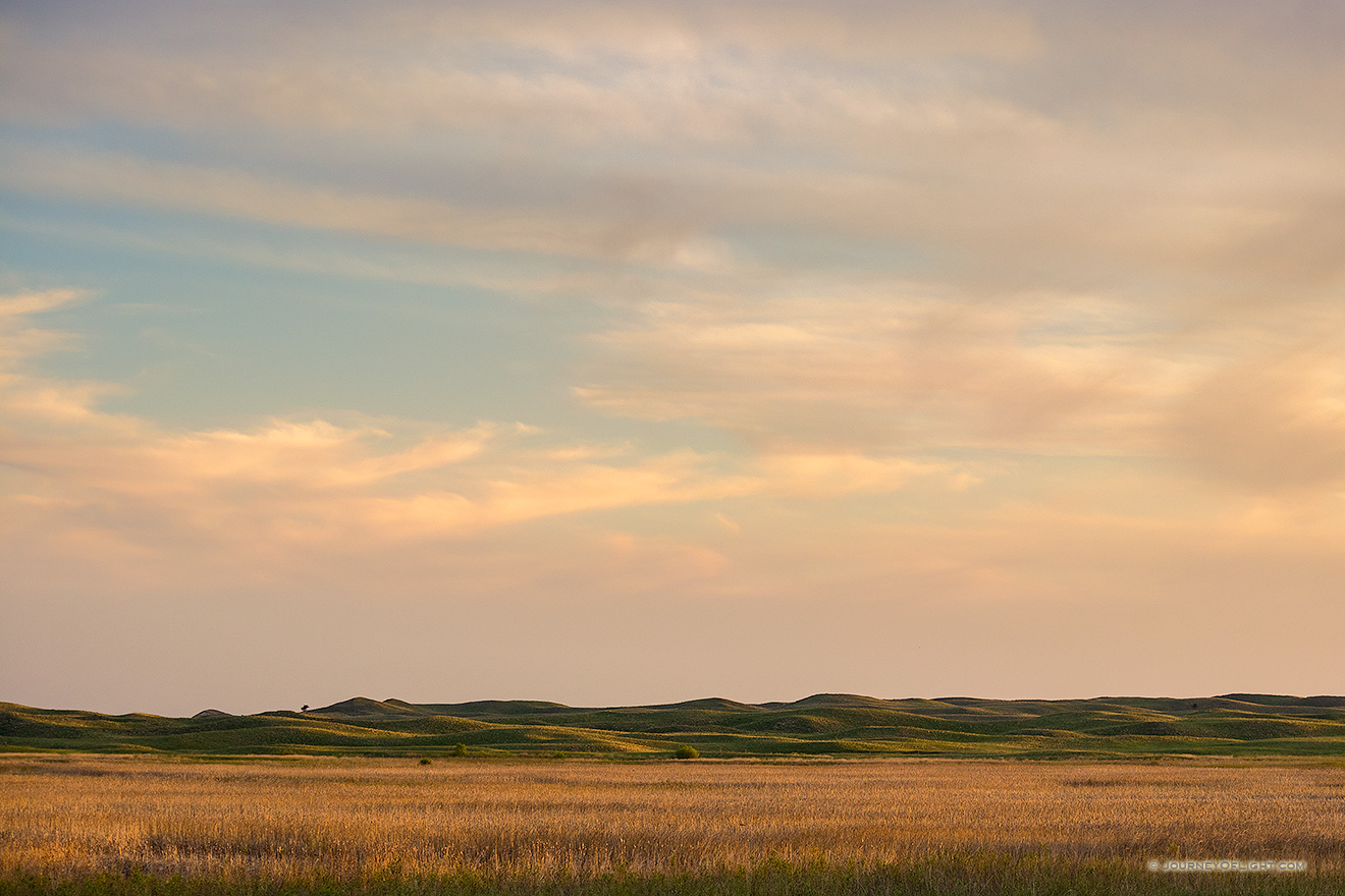 The last light of sunset skims across the Nebraska Sandhills and casts a warm glow on the clouds above.