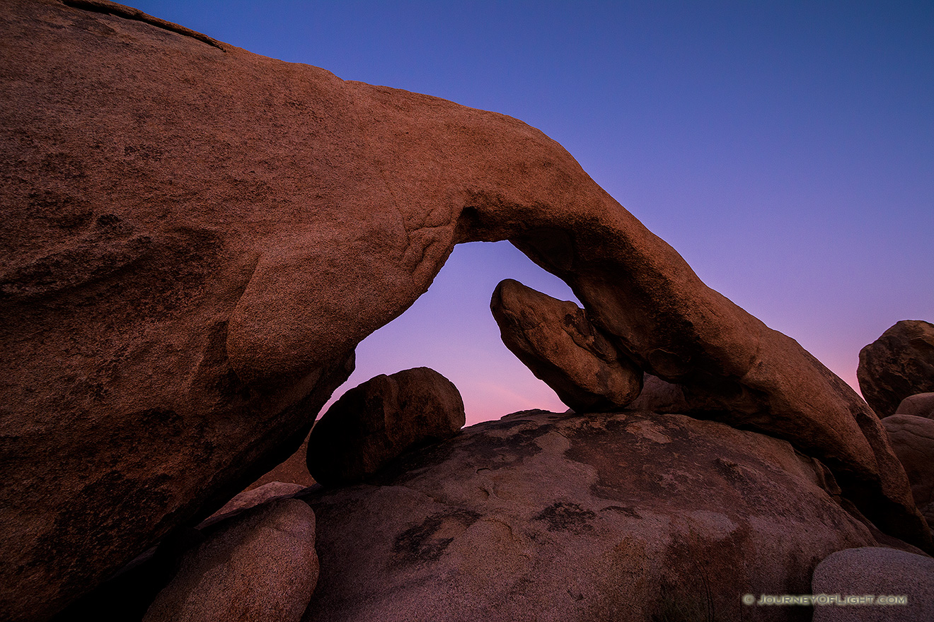 The sky takes on a deep purple hue over the natural arch in Joshua Tree National Park. - State of California Photography