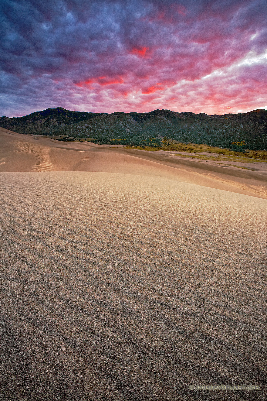 Early morning on the Great Sand Dunes after a stormy night brought clouds that reflected intense warm hues from the rising sun.  I had envisaged a photograph like this at the sand dunes for over a year, capturing the the texture of the dunes, the sweeping lines that lead to the Sangre de Cristo mountains, with a brillant sunrise. - Great Sand Dunes NP Picture