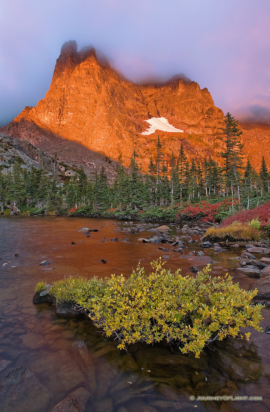 One of my favorite lakes in Rocky Mountain is Lake Helene.  About 2 and a half miles from Bear Lake, this spot is nestled at the bottom of Notchtop Mountain.  On a September day, the leaves on the bushes have turned a bright crimson hue and the early morning fog begins to dissipate quickly as the the mountain glows with the advent of a new dawn.  It is serenity and peacefulness with only the rustling of the trees and the occasional chirp of a Stellers Jay. - Rocky Mountain NP Picture