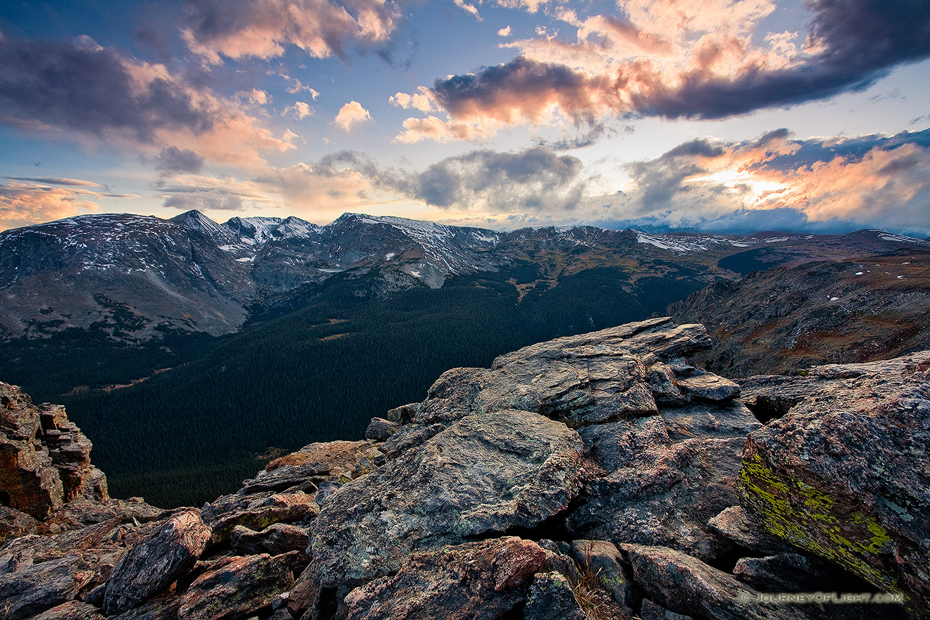 The setting sun streams through the clouds, illuminating the peaks of Rocky Mountain National Park and the valley below. - Colorado Picture